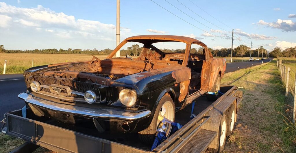 A 1965 Mustang on a flat bed trailer that needs to be restored by Leven Restorations