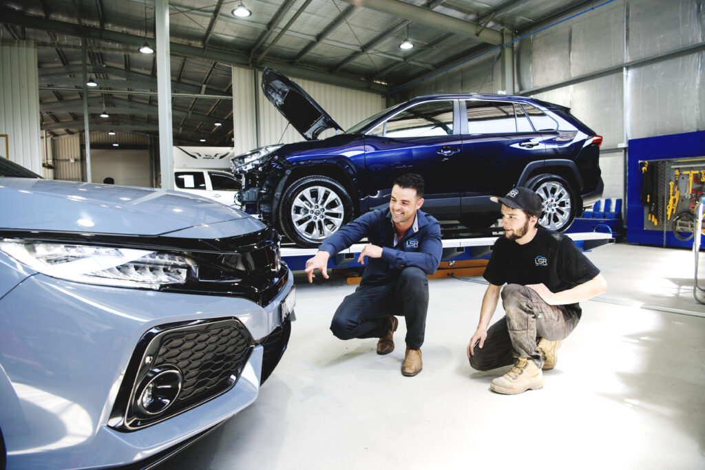 Two panel beaters reviewing a repaired car